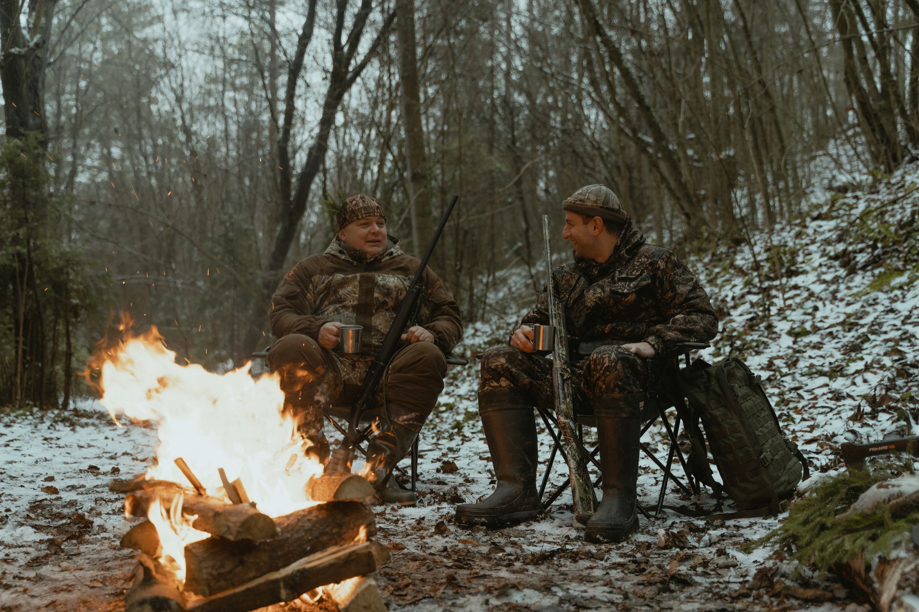 Two hunters warming by a campfire in the mountains